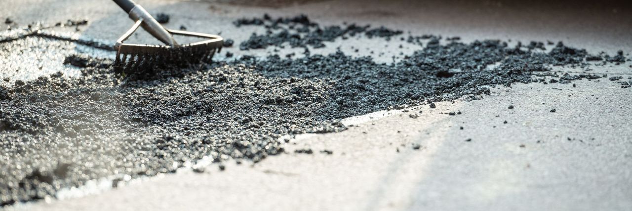 A rake spreading fresh black asphalt across a patch in a light concrete surface