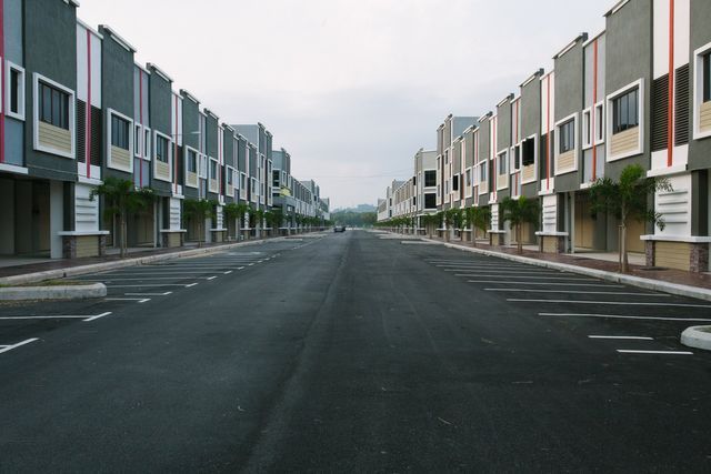 A newly paved street with marked parking bays running between two rows of shop units